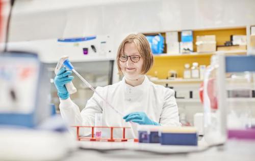 Smiling female researcher wearing glasses uses pipette controller in labratory