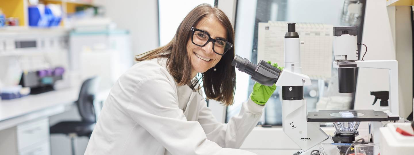 Smiling female researcher wearing glasses and green gloves using microscope