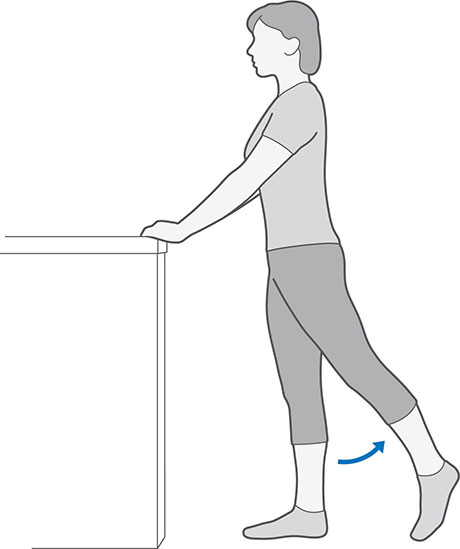 An illustration of someone standing whilst holding onto a table, moving their leg backwards and keeping it straight.