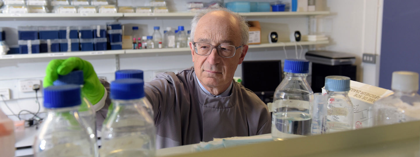 A researcher in a laboratory looking at clear liquid in a bottle.