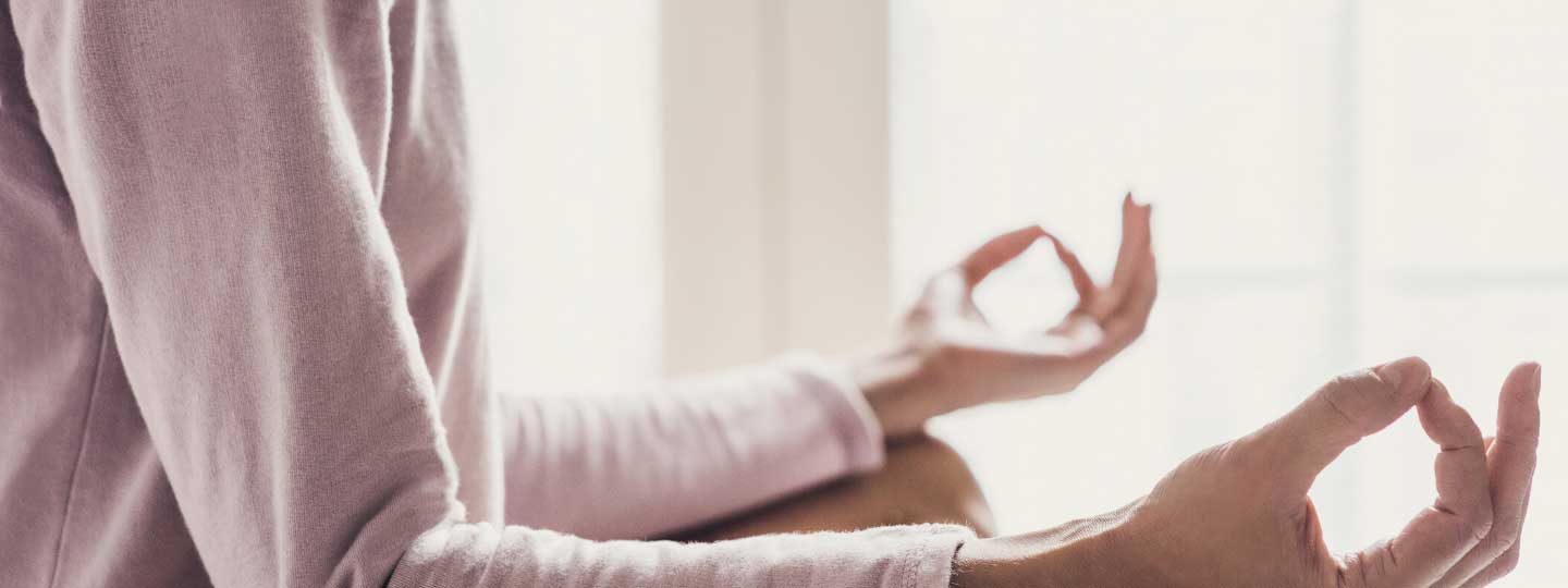 A lady meditating and holding her fingers in a relaxing yoga pose.