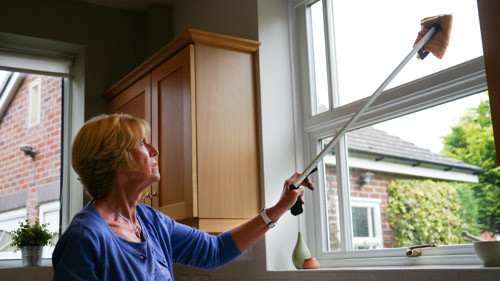 A lady using a pick up stick to clean the windows.