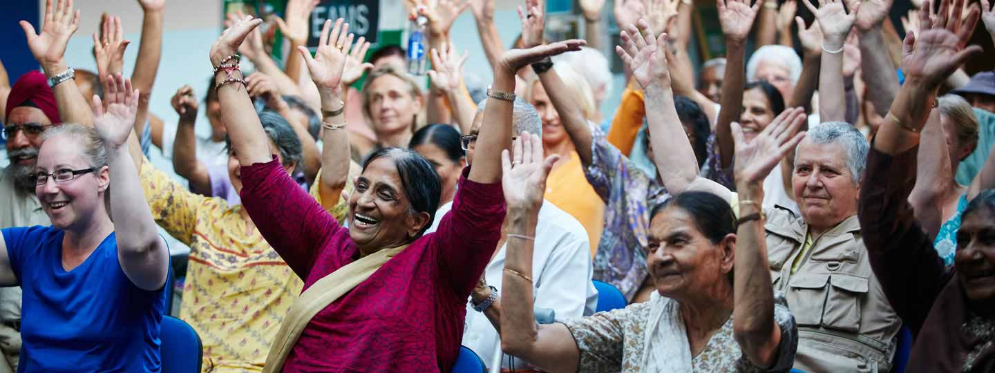 Diverse group of people sitting down with hands raised and smiling