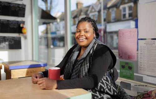 Smiling Monique sitting at a cafe table which has a red cup sat on top