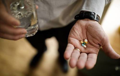 Hand holding several tablets and a glass of water