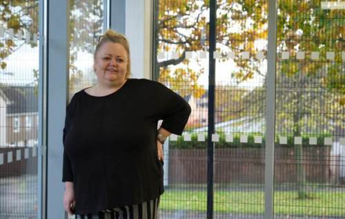 Smiling Tracey standing beside window overlooking green space