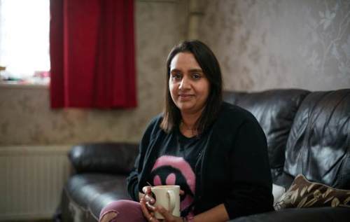 Smiling Priti holding a white mug sat in our living room sofa