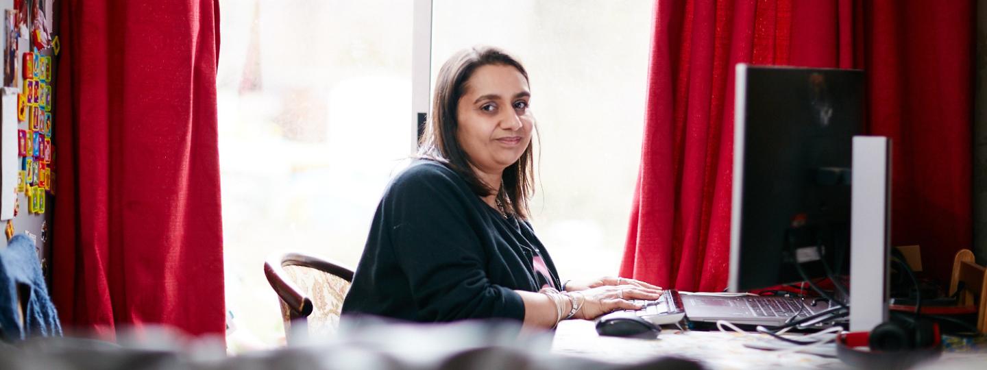 Smiling Priti sitting in her living room using her computer