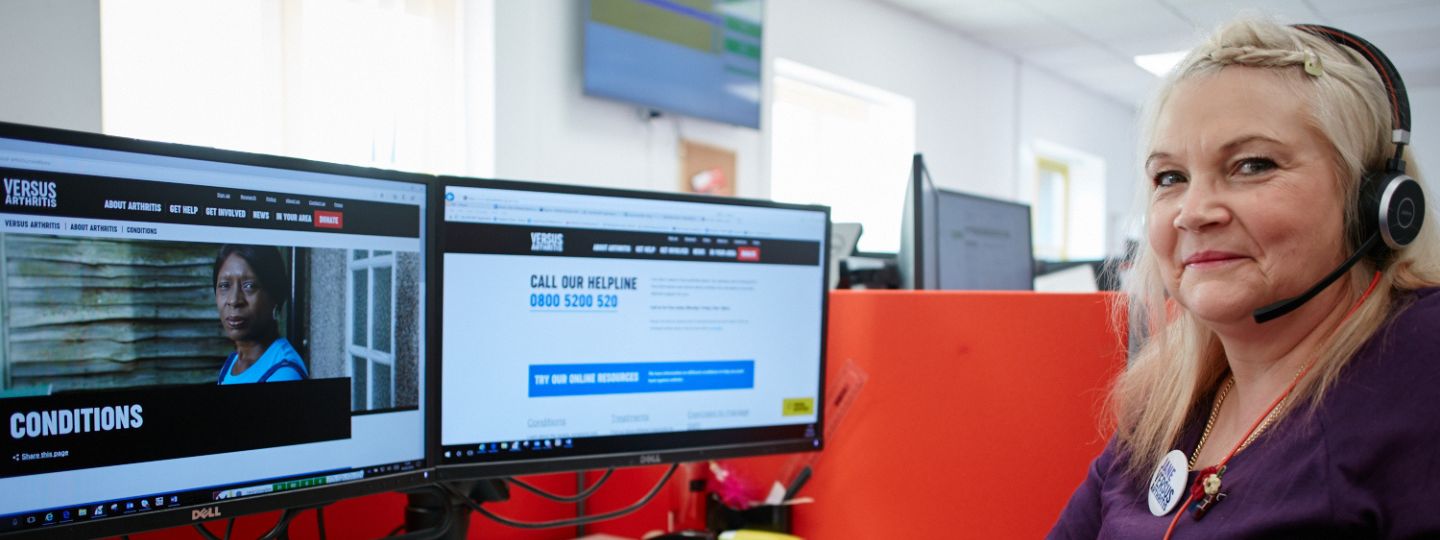 Smiling Helpline Advisor wearing headset sat at a computer