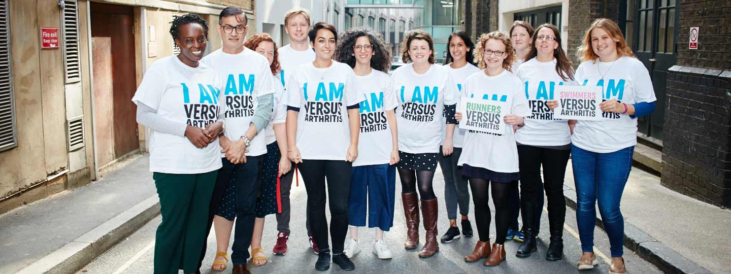 A group of people wearing Versus Arthritis t-shirts and holding signs.