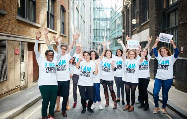 A group of people wearing Versus Arthritis t-shirts and holding signs.
