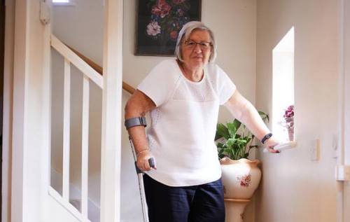 Christine wearing white t-shirt using a crutch while walking downstairs