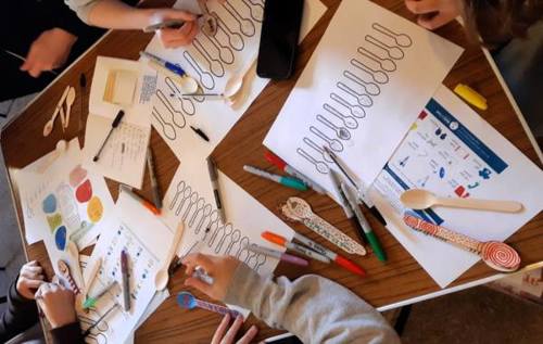 A group of young people colouring in sheets of paper illustrating spoons or wooden spoons