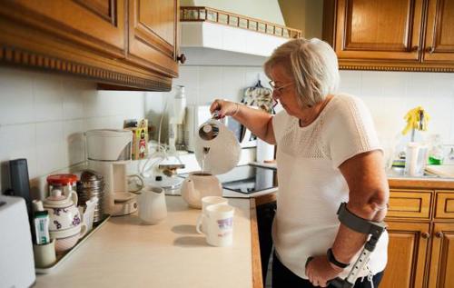 Christine using crutch in kitchen pouring kettle