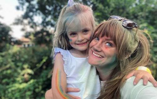 Zoe holding Mali and smiling while wearing colourful rainbow face paint