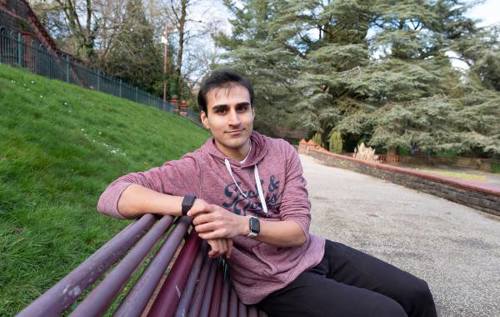 Rhys wearing red hoody sitting on park bench