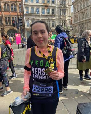 Smiling Megan wearing Versus Arthritis running vest holding London Landmarks medal and a bottle of water