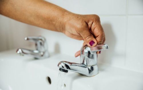 Woman turning lever tap wearing purple nail polish