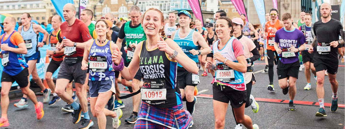 Smiling Ellana running with her thumbs up at the TCS London Marathon wearing a Versus Arthritis vest