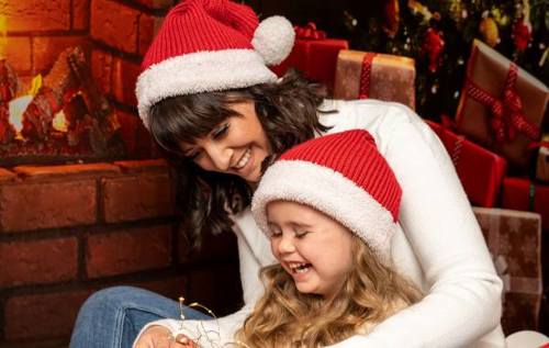 Linzie and Mia wearing Christmas hats cuddling by a fire