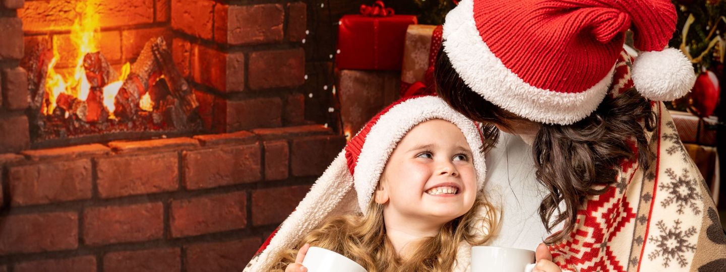 Linzie and Mia wearing Christmas hats cuddling by a fire