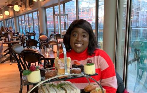 Melissa smiling in a restaurant, which has an afternoon tea on the table packed with sandwiches and cakes.