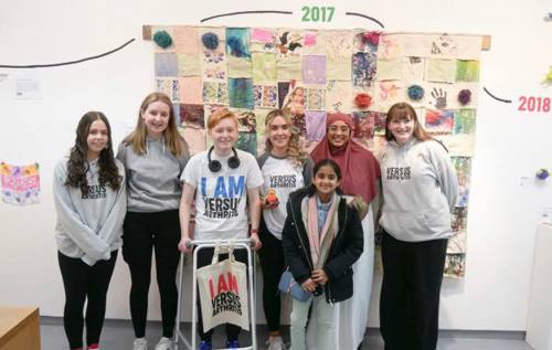 Group of young people wearing Versus Arthritis t-shirts standing in front of artwork