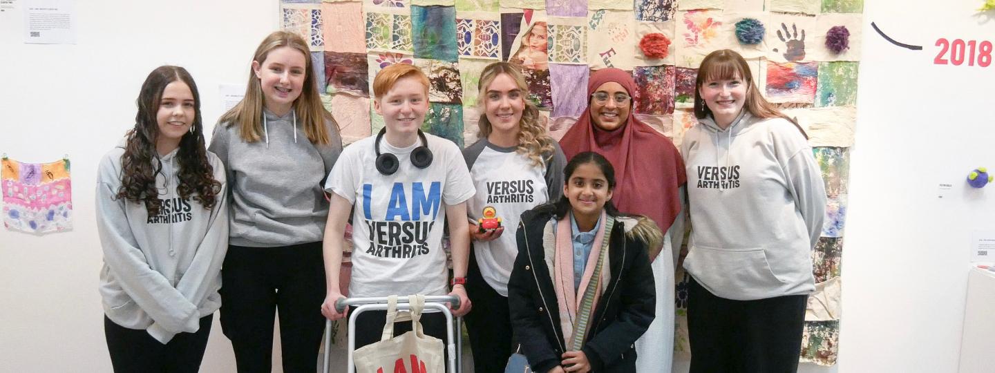 Group of smiling young people wearing Versus Arthritis t-shirts at the Joint Creativity art exhibit