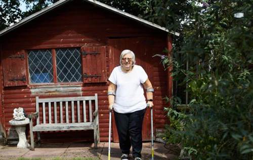 Christine using crutches in the garden in front of garden shed